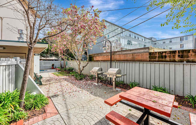 A patio with a picnic table and a tree with pink flowers.
