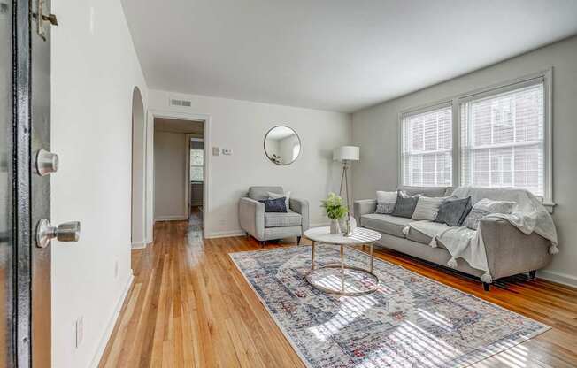 A living room with a grey couch and a round table with a vase of flowers on it.