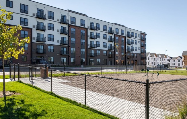 A black fence surrounds a playground in front of a multi-story apartment building.