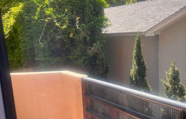 A balcony with a metal railing and a view of a building and trees.