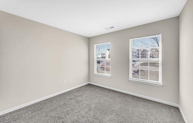 an empty room with carpet and two windows