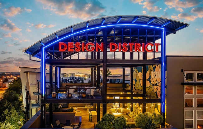 A modern building with a glass facade and a blue neon sign that reads "Design District".