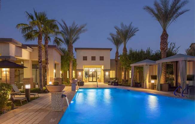 A pool surrounded by palm trees and a building in the background.