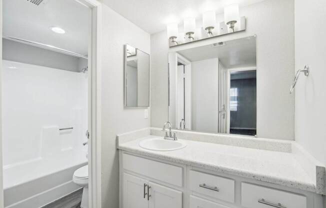 A white bathroom with a sink, mirror, and toilet.