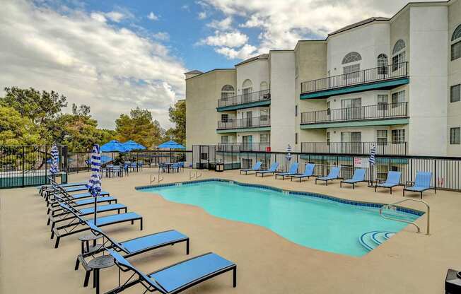 A swimming pool surrounded by sun loungers and apartment buildings.