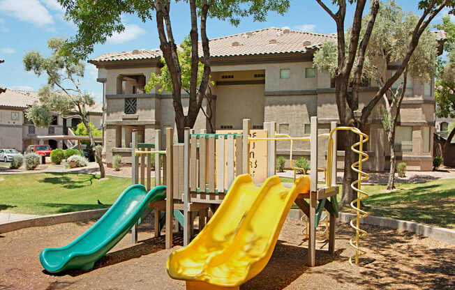 A playground with a green and yellow slide in front of a building.