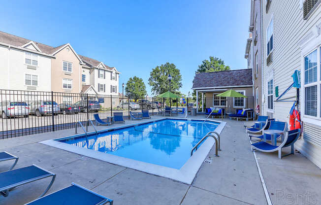 A swimming pool with lounge chairs and umbrellas is surrounded by apartment buildings.