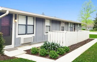 A small building with a grey siding and a white picket fence.