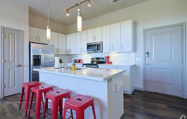 A kitchen with white cabinets and a white island with red stools.