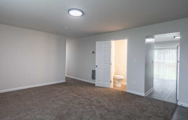 an empty living room with a door to a bathroom and a toilet