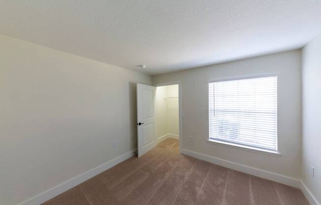 A room with a carpeted floor and a window with blinds.