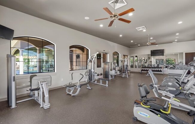 a gym with various exercise machines and a ceiling fan