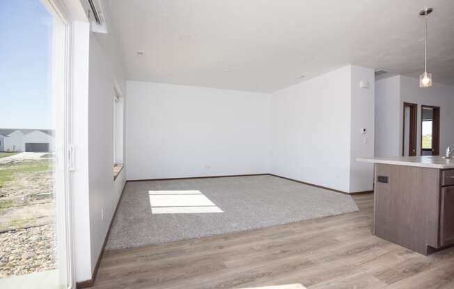 an empty living room with a kitchen and a window