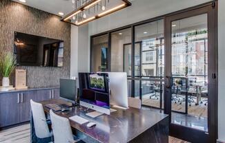 Pet Friendly Apartments in Grand Prairie, TX - Waters Edge at Mansfield - Private Business Center With Table, Chairs, Computers, Mounted TV, Pendant Light Fixture, and Puck Lighting.