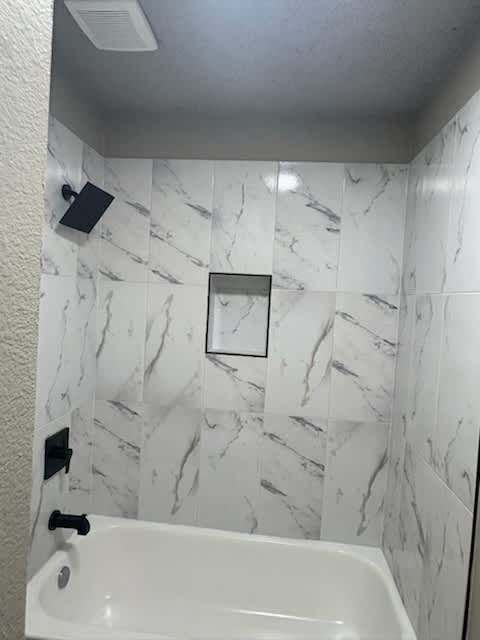 A white bathroom with a marble tile wall and a white tub.