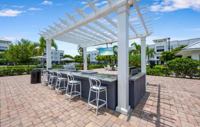 an outdoor bar with white columns and a white pergola on top of a brick patio