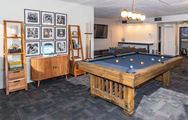 A pool table in a room with a wooden cabinet and a wall of framed pictures.