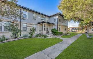 a sidewalk in front of a building with grass and trees  at Sunset Ridge, San Antonio, 78209