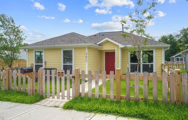 A yellow house with a red door and a wooden fence.