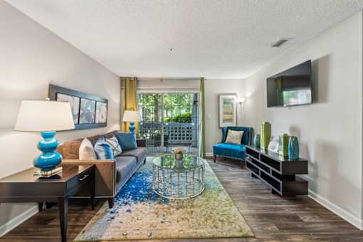 A living room with a blue rug and a glass table.