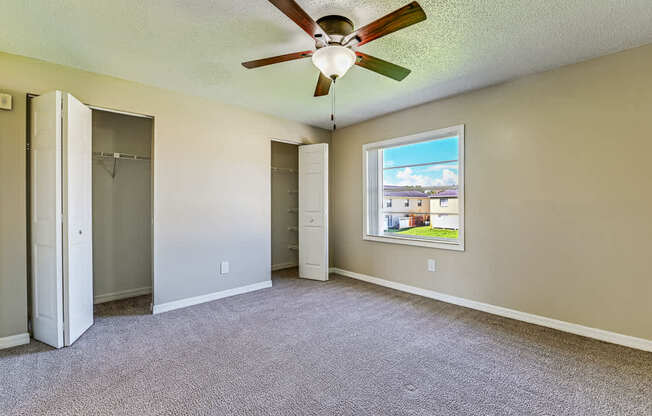 A room with a ceiling fan and a window showing a view of a house.