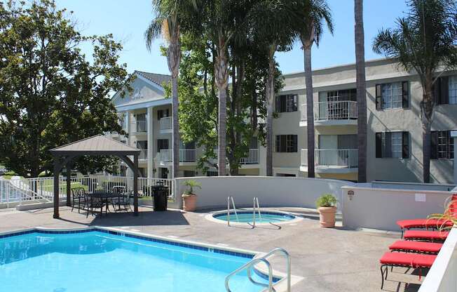 A pool with red chairs and a building in the background.