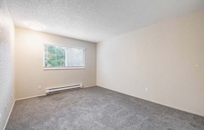 Bedroom with a large window, baseboard heater, and carpeted flooring in a two-bedroom apartment at Peak 88 in Renton, WA.
