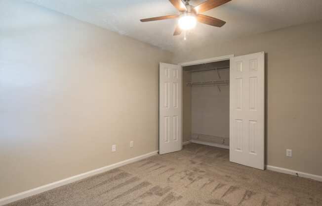 an empty bedroom with a ceiling fan and a closet