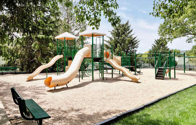 A playground with a yellow slide and a green bench.