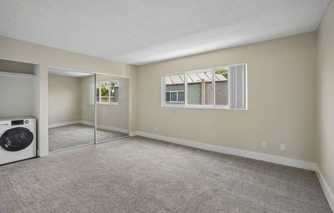 A room with a carpeted floor and a window with a view of a building.