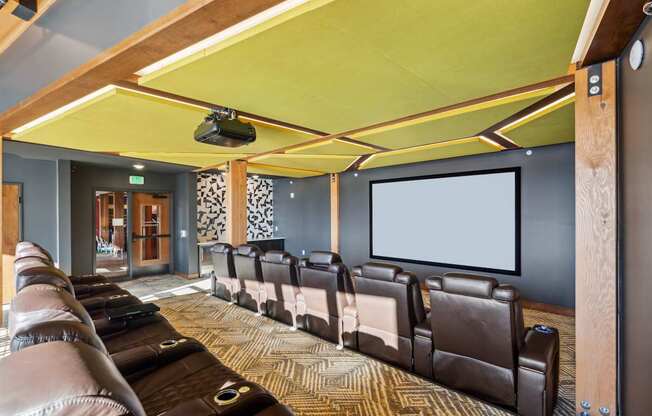 A home theater with a row of brown leather chairs and a large screen.