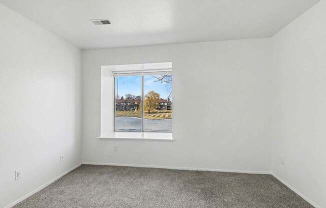 A bedroom with a large window showing a view of a pond at Trappers Cove Apartments, Lansing
