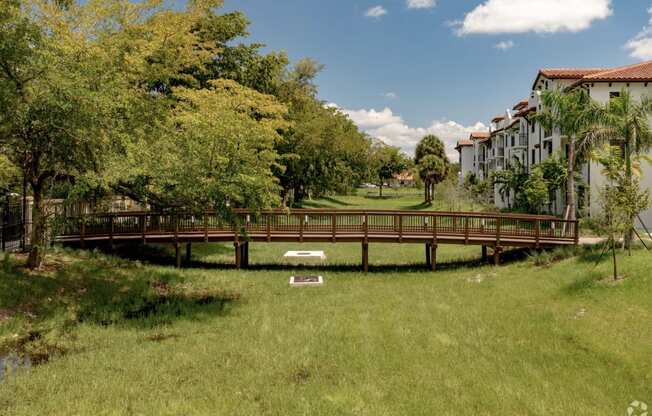 a bridge over a grassy area with trees and buildings in the background