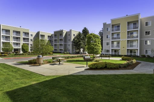 an open area with benches and trees in front of an apartment building  at Camelot Apartment Homes, Everett