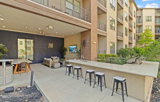 A patio with a bar and stools is surrounded by apartment buildings.
