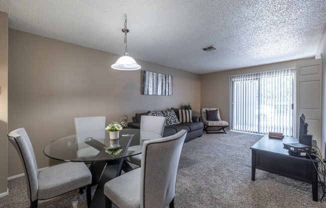 A living room with a glass table and grey chairs.
