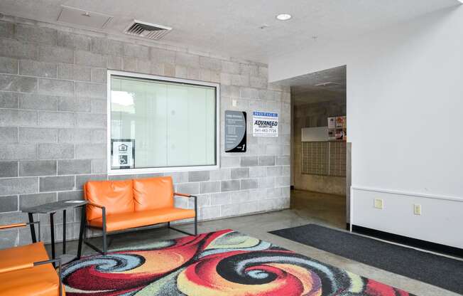 a lobby with orange chairs and a colorful rug and a window