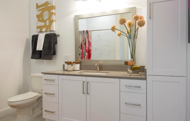 A bathroom vanity with a quartz countertop, white cabinets and drawers below the sink, and cabinets up to the ceiling beside the vanity.