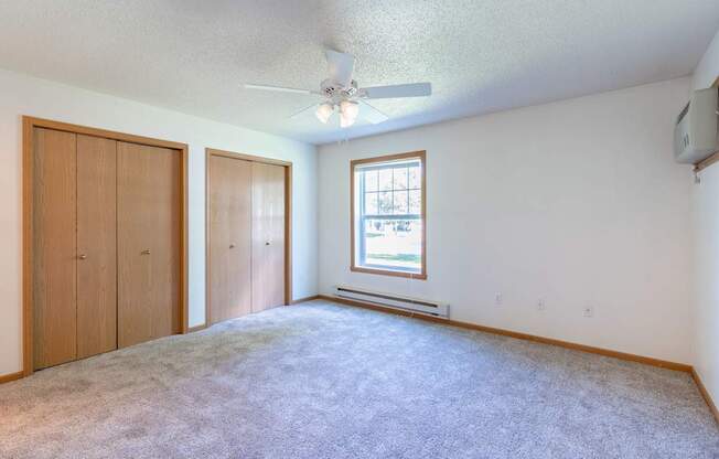 A room with a carpeted floor, a ceiling fan, and a window with blinds. Fargo, ND Stonebridge Apartments