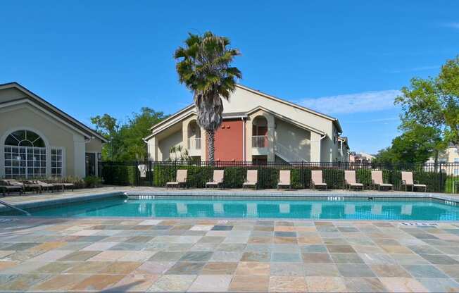 A swimming pool surrounded by a stone patio and a house with a palm tree in front.