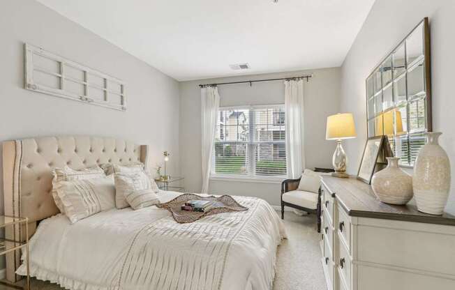 A bedroom with a large bed, a nightstand, and a window with curtains.