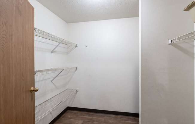 an empty closet with white walls and shelves and a wooden door. Fargo, ND Oxford Apartments