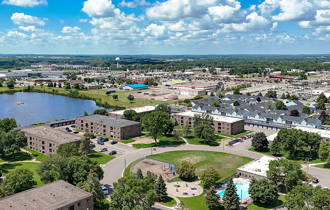 A large building complex with a pool in the middle of a green area.