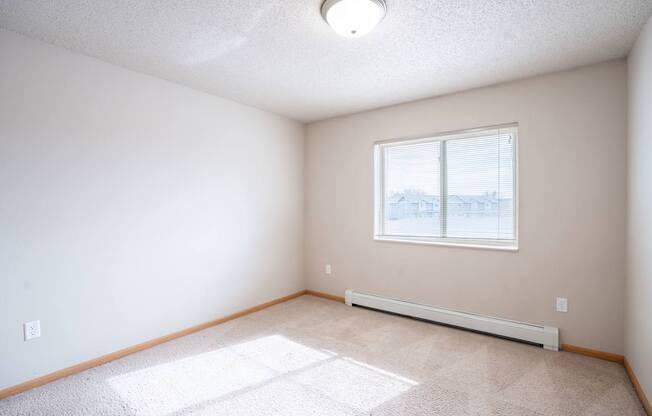 A room with a window and a carpet on the floor. Fargo, ND East Bridge Apartments