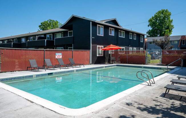 A swimming pool in front of a building with a red umbrella.