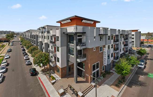 A street view of a residential area with apartment buildings and cars parked on the side of the road.