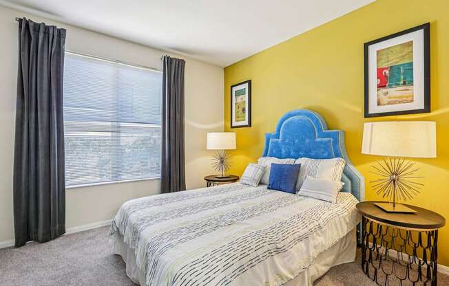 A bedroom with a bed, two lamps, and a window with curtains.