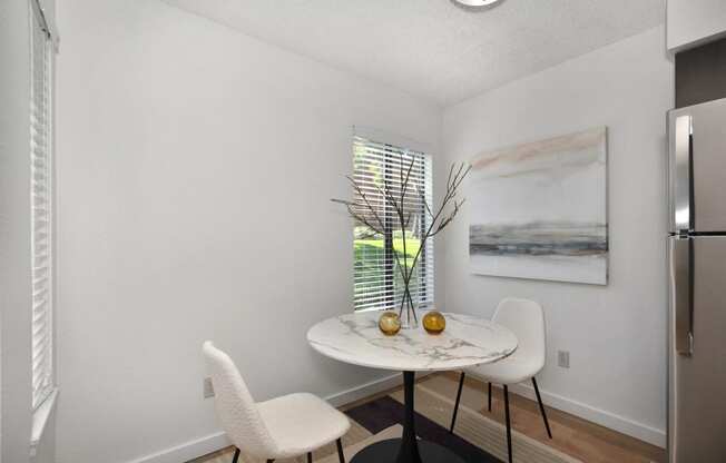 a small dining room with two white chairs and a marble table with two vases on it