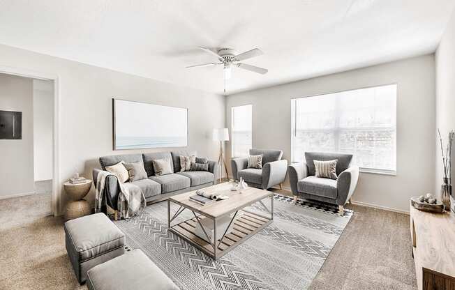 Virtually staged living room with carpet, accent rug, gray couches and seating, tan coffee table, ceiling fan, large windows