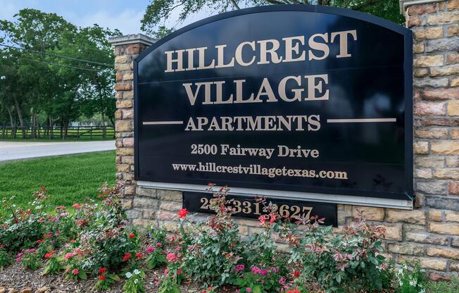 Sign for Hillcrest Village Apartments located at 2500 Fairway Drive, featuring a decorative stone base and surrounded by flower beds.